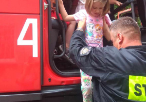 Strażak pomaga dzieciom wysiąść z kabiny wozu strażackiego.