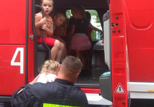 Strażak pomaga dzieciom wejść do kabiny wozu strażackiego.