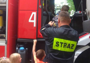 Strażak pomaga dzieciom wsiąść do kabiny wozu strażackiego.