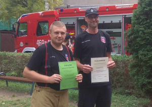Przewdstawiciele Ochotniczej Straży Pożarnej trzymają w rękach podziękowanie i dyplom, które otrzymały od przedszkolaków.