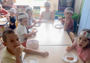 Dzieci jedzą pizzę przy stolikach.
