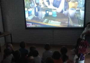 Dzieci oglądają film instruktażowy, dotyczący przesadzania roślin.