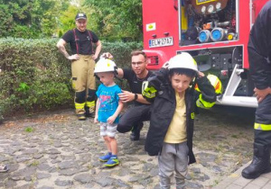 Dzieci mierzą kurtkę i hełm strażacki.