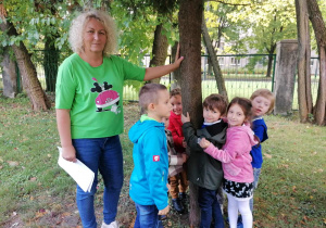 Dzieci wraz z nauczycielem dotykają korę drzewa.