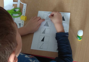 Chłopiec dokleja na kartce pasujący trójkąt.