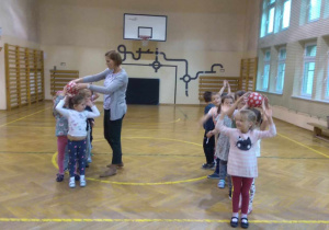 Dzieci w dwóch drużynach przekazują sobie piłki z rąk do rąk nad głowami.