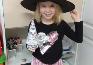 Dziewczynka w kapeluszu czarownicy pokazuje czarownicę wykonaną z papieru.