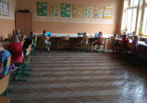 Dzieci siedzą przy stanowiskach komputerowych.
