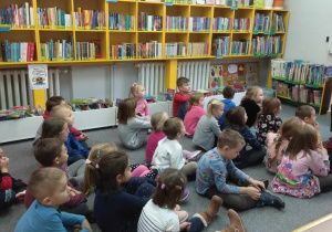 Dzieci siedzą na dywanie i słuchają opowieści Pani bibliotekarki.