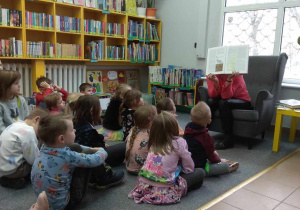 Dzieci siedzą na dywanie i słuchają opowieści Pani bibliotekarki.