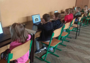 Dzieci siedzą przy komputerach i grają w gry edukacyjne.