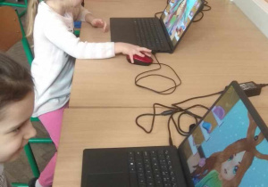Dzieci siedzą przy komputerach i grają w gry edukacyjne.