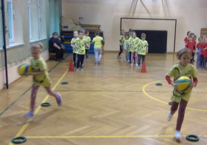 Dzieci biegną z piłkami po wyznaczonej trasie.