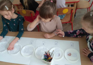 Dzieci w małych zespołach kolorują elementy z matematycznego zadania.