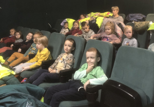 Dzieci pozują do zdjecia na kinowych fotelach.