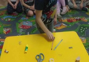 Na stoliku leżą przedmioty z różnego rodzaju materiału: plastiku, drzewa, metalu. Dzieci sprawdzają, co przyciągnie magnes.