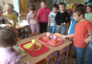 Dzieci obserwują i podziwiają kolorowe wybuchy wulkanów - efekt po dodaniu do mikstury octu.