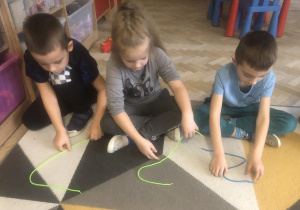 Dzieci układają literę ze sznurka.