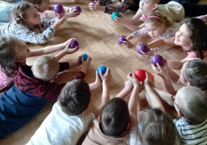 Dzieci wykonują ćwiczenia z wykorzystaniem plastikowej piłki.