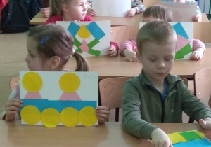 Dzieci prezentują swoje prace, wykonane z figur geometrycznych.