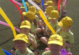 Dzieci siedzą na boisku CHKS, trzymają w rękach balony i oczekują na rozpoczęcie Spartakiady.