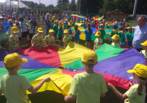 Dzieci trzymają chustę animacyjną, w środku jest 1 piłeczka, która ma wypaśc przez otwór w chuście.