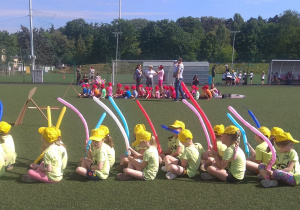 Dzieci siedzą na boisku CHKS, trzymają w rękach balony i oczekują na rozpoczęcie Spartakiady.