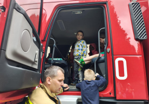 Dzieci wsiadają do wozu strażackiego.