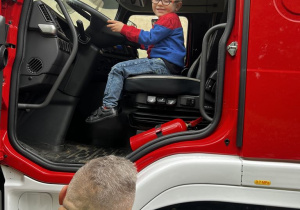 Dziecko ogląda kabinę wozu strażackiego.