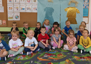 Dzieci siedzą na dywanie, za nimi widać wykonane postaci z odrysowanych dzieci.