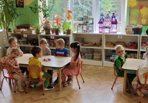 Dzieci siedzą przy stolikach i jedzą babeczki.