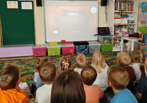 Dzieci siedzą na dywanie i oglądają film "Kodeks zachowania z psem".