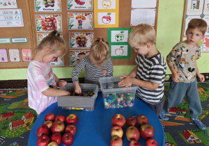 Dzieci wybierają guziki i pompony do wypełnienia kolorowych konturów jabłek.