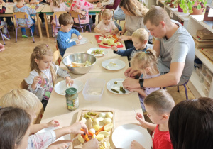 Dzieci przy pomocy rodziców wykonują sałatkę jarzynową.