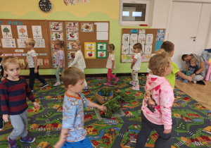 Na dywanie stoi kosz pełen warzyw, dzieci maszerują w koło i spiewają wesołą piosenkę.