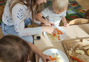 Dzieci przy pomocy rodziców wykonują sałatkę jarzynową.