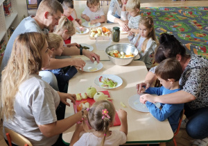 Dzieci przy pomocy rodziców wykonują sałatkę jarzynową.