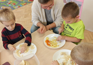 Dzieci przy pomocy rodziców wykonują sałatkę jarzynową.