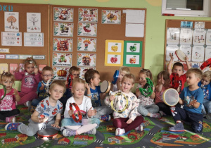 Dzieci siedzą na dywanie trzymając w rękach instrumenty.