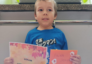 Chłopiec trzyma w rękach dyplom i stworzoną przez siebie książeczkę.