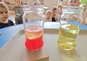 Dzieci obserwują zmiany zachodzące w słoiku po dodaniu musującej tableki.