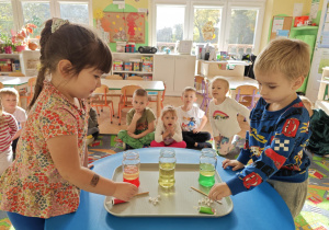 Dzieci obserwują zmiany zachodzące w słoiku po dodaniu musującej tableki.