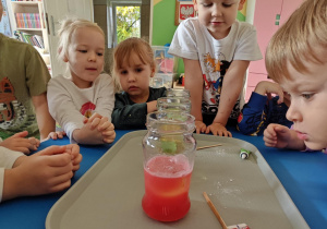 Dzieci obserwują zmiany zachodzące w słoiku po dodaniu musującej tableki.