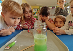 Dzieci obserwują zmiany zachodzące w słoiku po dodaniu musującej tableki.