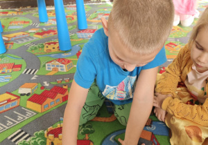 Dziecko rozpoznaje za pomocą dotyku jaki pomarańczowy owoc lub warzywo ukrył się w torebce.