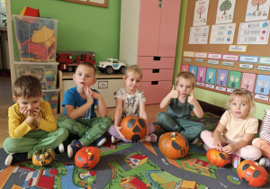 Dzieci siedzą przy swoich ozdobionych dyniach.