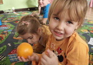 Dziecko rozpoznaje za pomocą dotyku jaki pomarańczowy owoc lub warzywo ukrył się w torebce.
