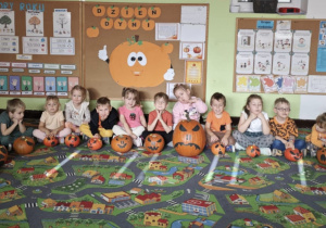 Dzieci siedzą przy swoich ozdobionych dyniach.