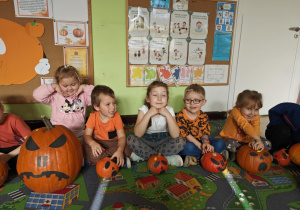 Dzieci siedzą przy swoich ozdobionych dyniach.