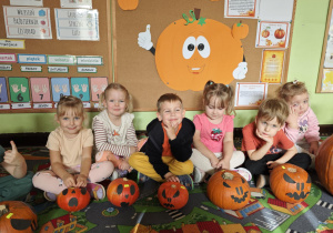 Dzieci siedzą przy swoich ozdobionych dyniach.